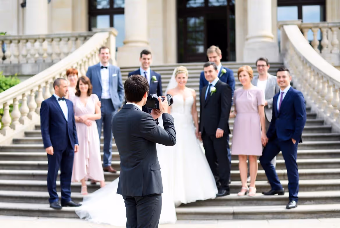 Wedding photographer directing a formal group portrait of bride, groom, and family on elegant stone steps